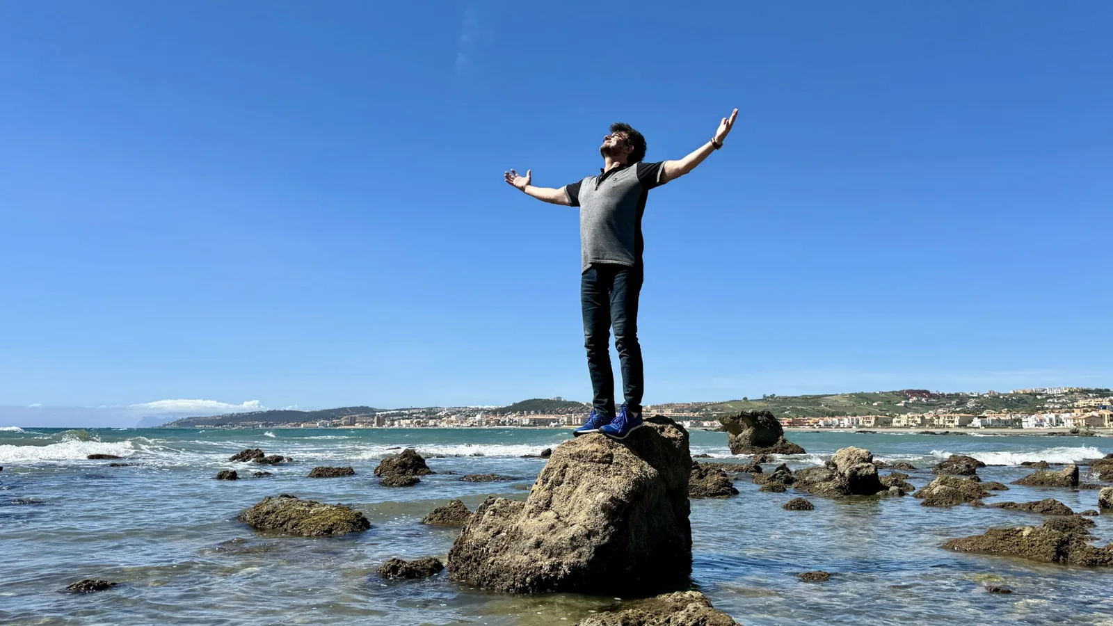 Justin Jernoiu mit ausgebreiteten Armen auf einem Felsen am Meer Justin Jernoiu mit ausgebreiteten Armen auf einem Felsen am Meer